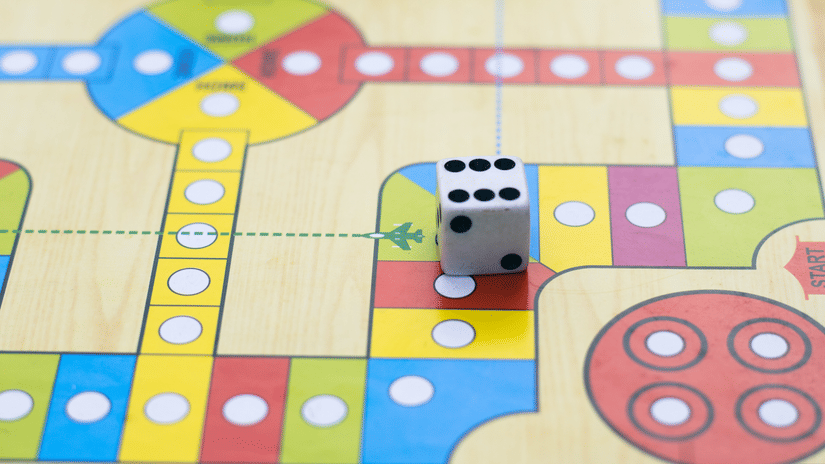 Colourful board game with a die showing a six, alongside playing pieces on a path with various coloured squares and circular spaces