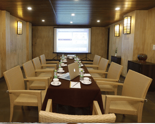 A conference room with a large table, chairs, and a projector screen, set for a business meeting
