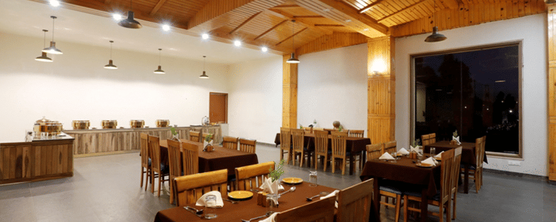 A spacious, well-lit restaurant or dining hall with wooden tables and chairs, ready for guests at Digantaa Resort