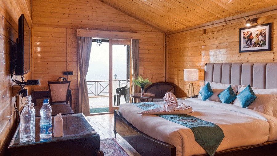 A well-appointed hotel room at Digantaa Resorts featuring wooden interiors, a king-sized bed with accents, and a balcony with a view